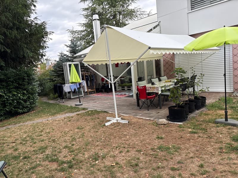 Garden area with a covered patio, outdoor dining table, chairs, potted plants, and a clothesline with laundry.