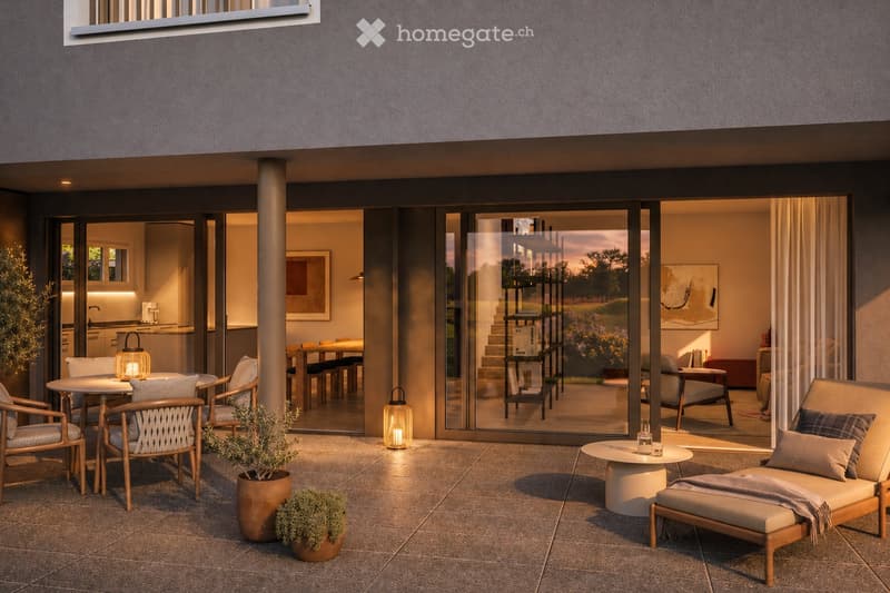 A modern outdoor patio with a tiled floor, featuring a round table with chairs, a lounge chair with an ottoman, potted plants, and lanterns. Large glass doors open to a well-lit interior with a dining area and kitchen visible.