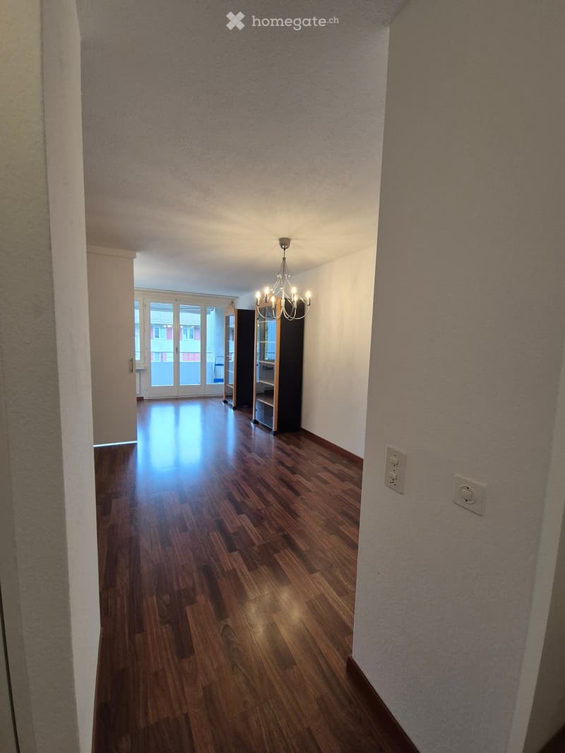 Empty room with wooden floor, chandelier, white walls, double doors with glass panels leading to balcony, electrical outlets.