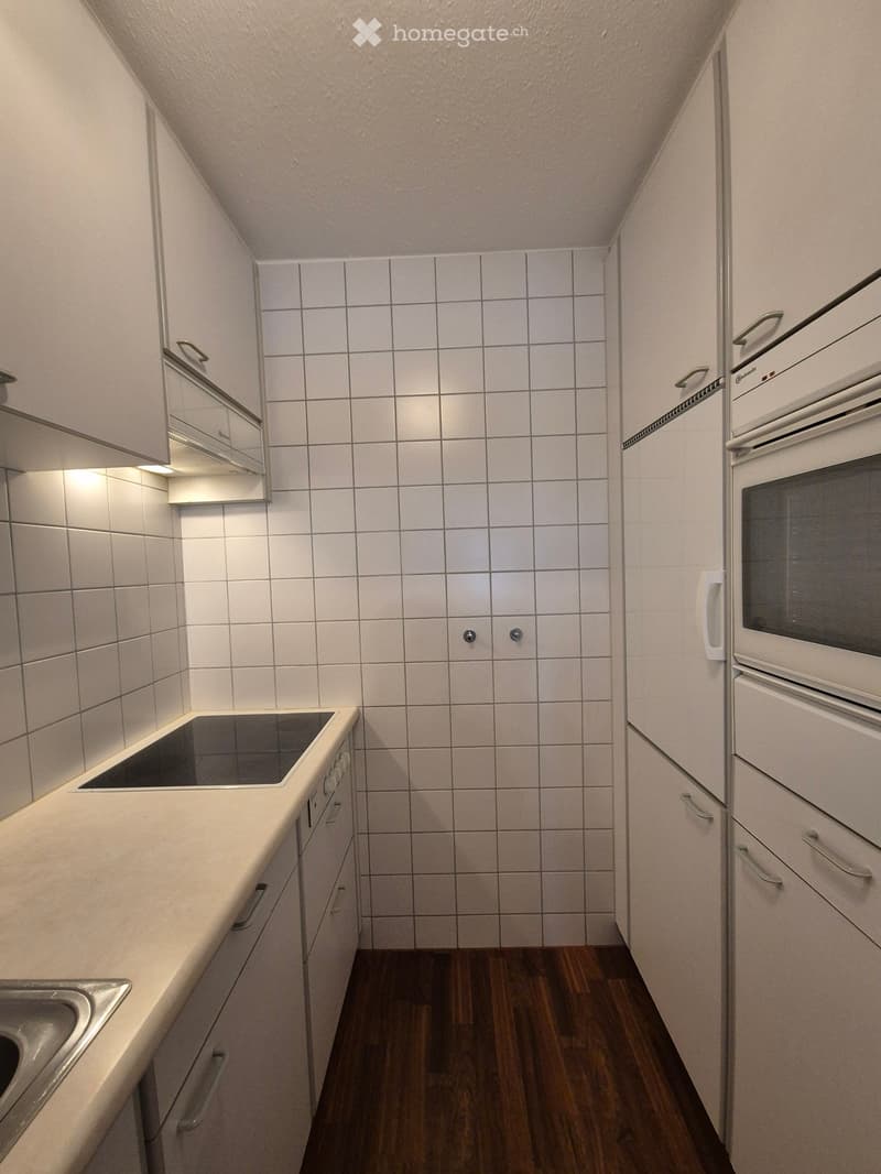 White tiled walls, wooden floor, countertop, electric stove, oven, dishwasher, refrigerator, and cabinets.