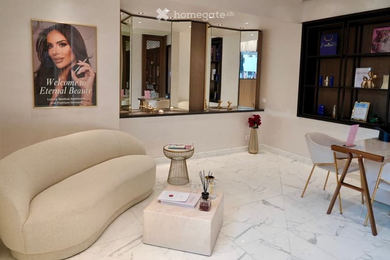 Modern, minimalist waiting area with a curved sofa, small round table, white chair, decorative items, and a large mirror. The space features marble flooring and elegant decor.