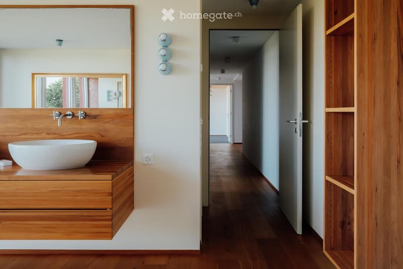 Bathroom with wooden vanity, white sink, mirror, wooden floors, and open hallway