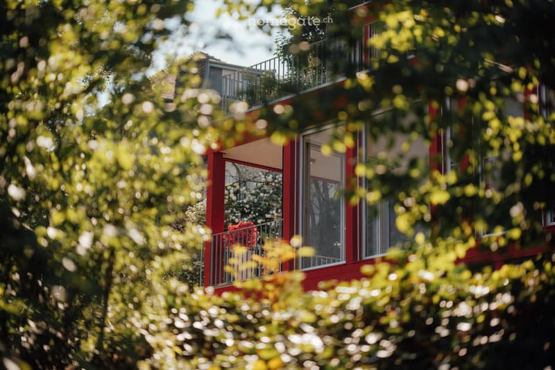red building, glass windows, balcony with metal railings, greenery