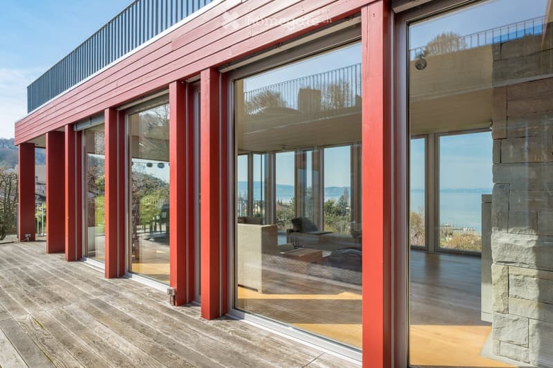 modern house, red exterior, large glass windows, wooden deck, balcony, sea view