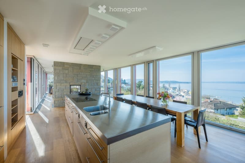 modern kitchen with large windows, stainless steel countertop, wooden dining table, view of the sea