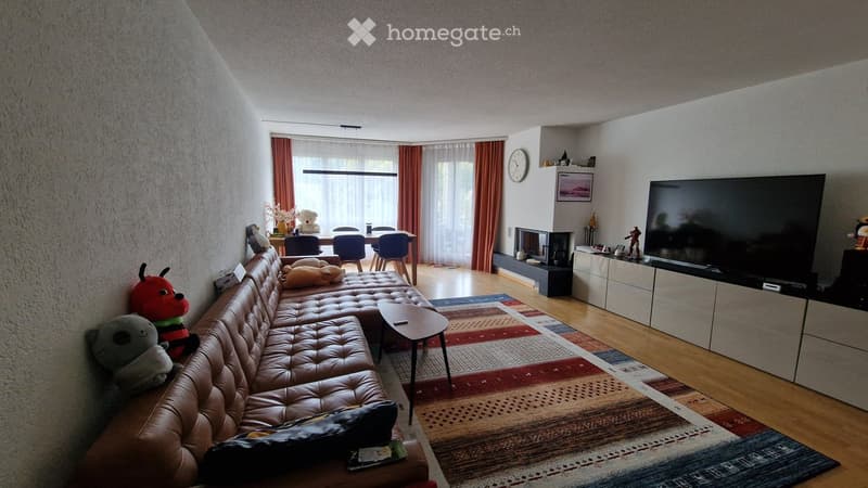 Modern living room with a leather sofa, coffee table, flat-screen TV, dining area with chairs, fireplace, and decorative items.