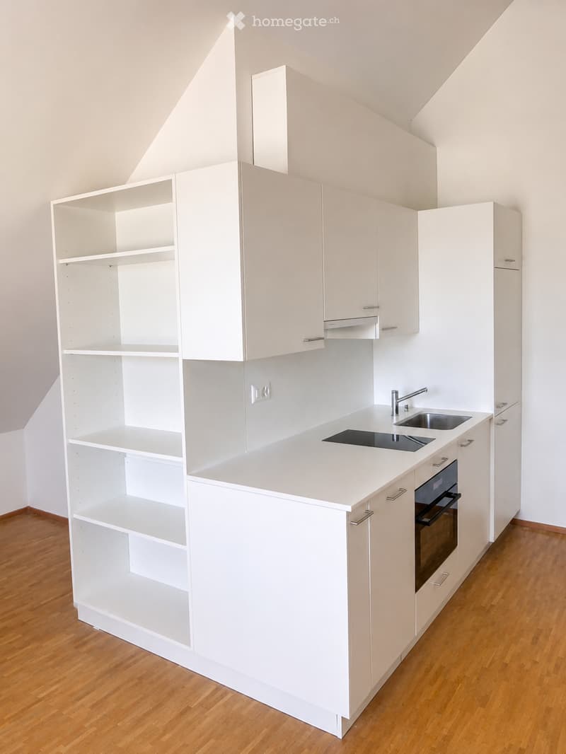 Modern, minimalist kitchen with white cabinets, a central island, and built-in appliances including a sink, faucet, and oven. The space features wooden flooring and ample shelving.