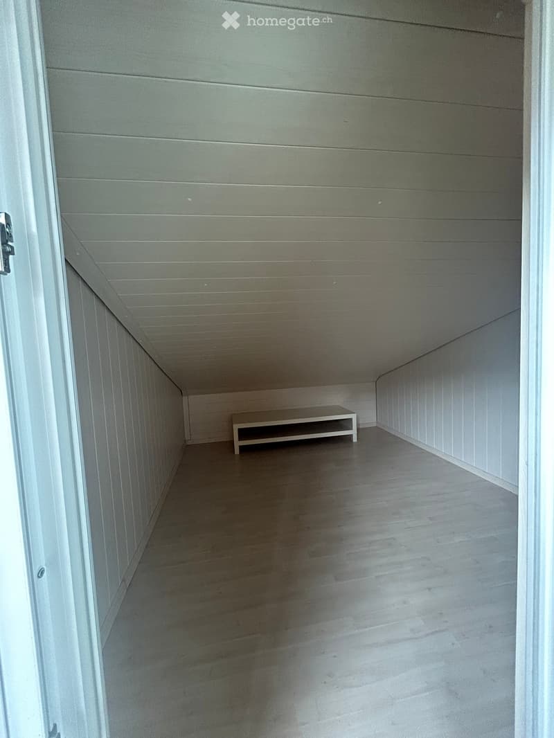 A narrow hallway with light wood paneling on the walls and ceiling, a small bench placed against the wall, and a polished concrete floor.