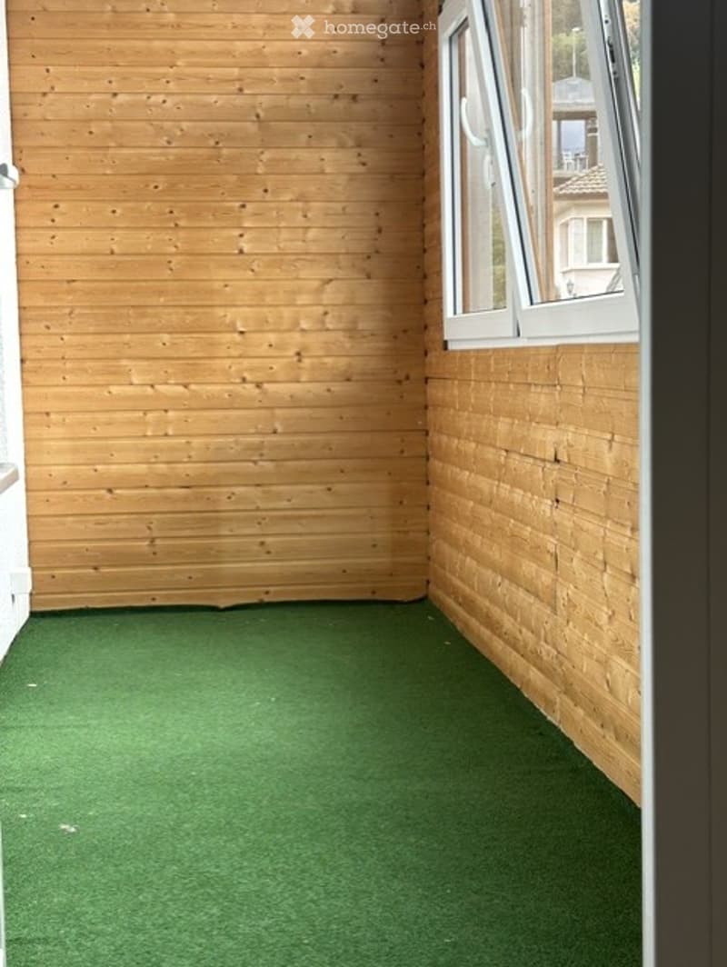 Empty room with wooden walls, green artificial turf flooring, and a large window offering a view of the outside.