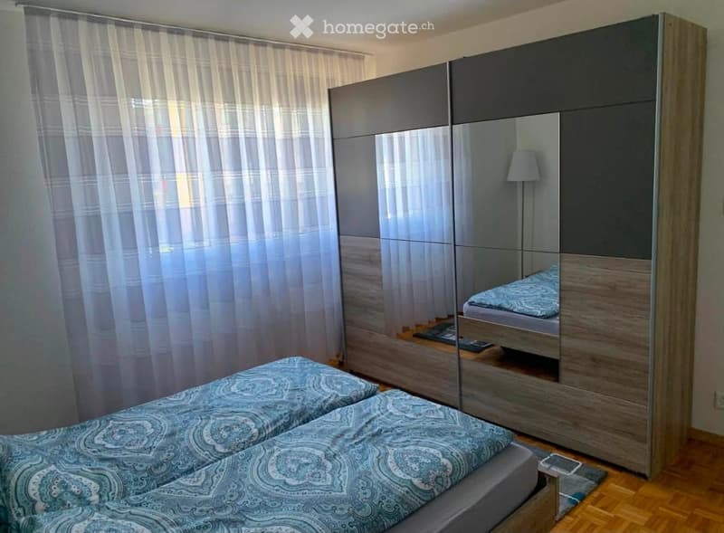 Modern bedroom with two single beds, a large mirrored wardrobe, and a lamp on the floor.