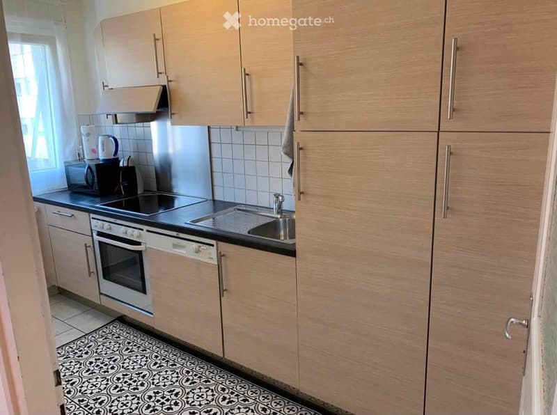 Modern kitchen with light wood cabinets, stainless steel appliances, and a black countertop. Features an oven, dishwasher, microwave, and a sink with a faucet.
