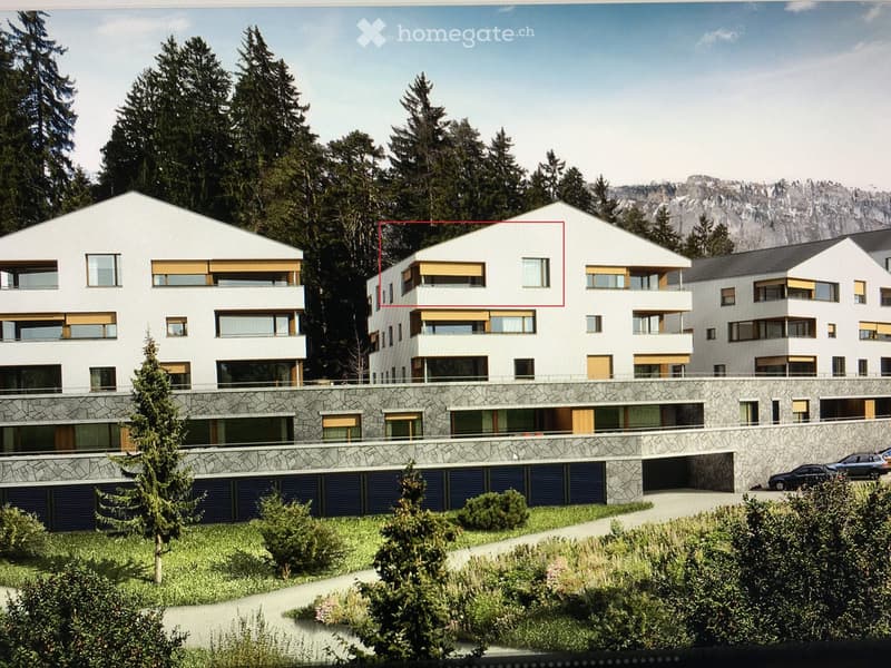 Modern multi-story residential building with white facade, large windows, balconies, and stone base. Surrounded by greenery and mountains.