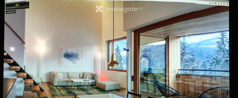 Modern living room with large windows offering a scenic mountain view, featuring a light-colored sofa, coffee table, ottoman, and pendant light.