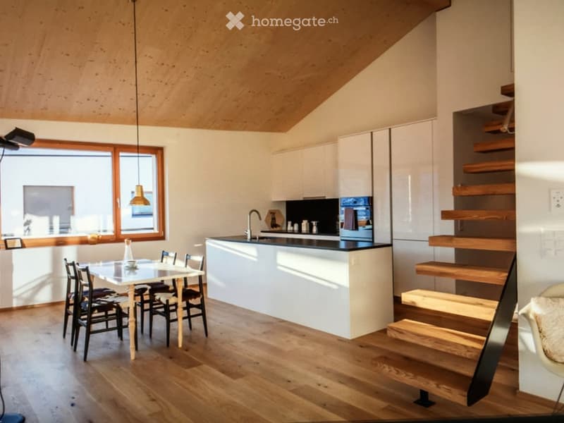 Modern kitchen and dining area with white cabinets, a central island, a dining table with chairs, and a staircase leading upwards.