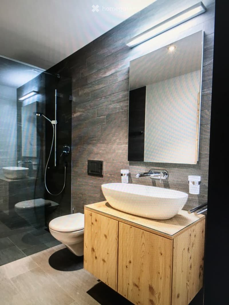 Modern bathroom with a wooden vanity, white sink, large mirror, and a glass-enclosed shower area.