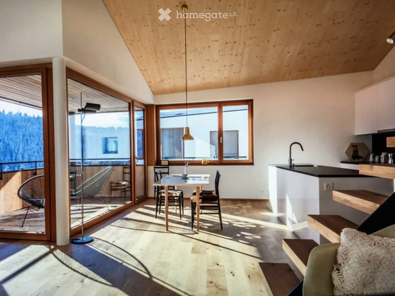 Open-plan living and dining area with large windows offering a scenic view, featuring a dining table with chairs, a modern kitchen counter, and a floor lamp.