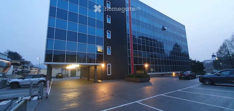 large building with glass windows, entrance with cars, parking area, several cars