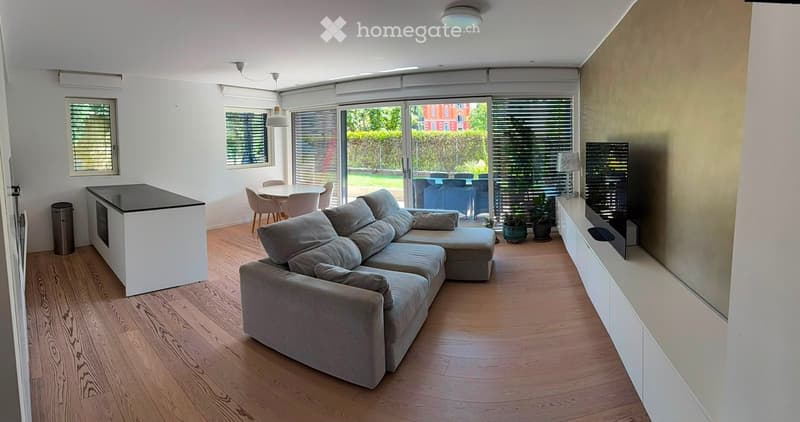 Modern living room with a grey sectional sofa, coffee table, TV stand, kitchen island, and dining area with chairs.