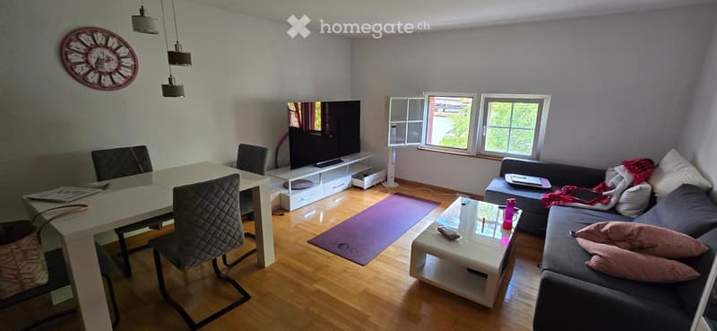 Living room with a grey sofa, coffee table, dining table, chairs, TV, and a yoga mat on the floor.