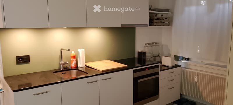 Modern kitchen with white cabinets, stainless steel sink, oven, toaster, and various small appliances on the counter.