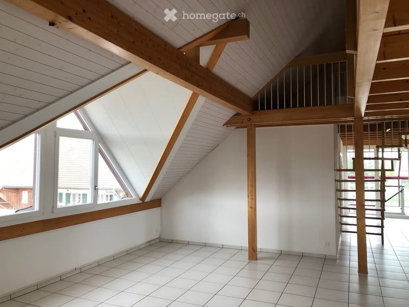 An empty attic space with exposed wooden beams, white walls, tiled floor, and a metal staircase leading to an upper level. Large skylight windows provide natural light.