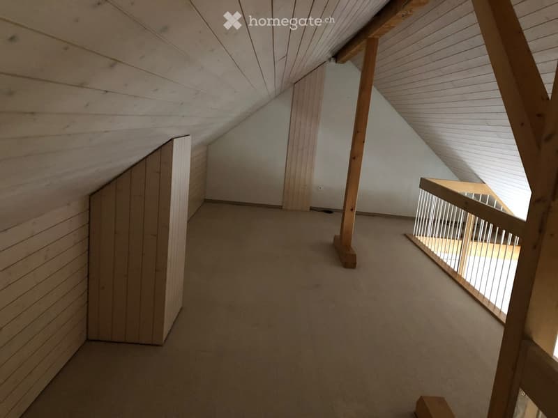 Empty attic space with wooden walls, slanted wooden ceiling, carpeted floor, and a staircase leading downwards.