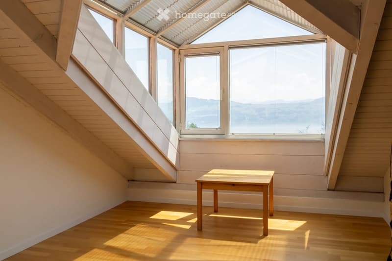 Bright, airy attic room with wooden floors, large skylight windows, and a simple wooden table.