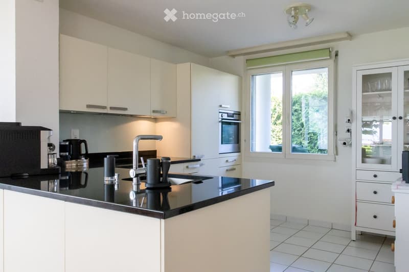 Modern kitchen with white cabinets, black countertop, stainless steel appliances, and a large window with blinds.