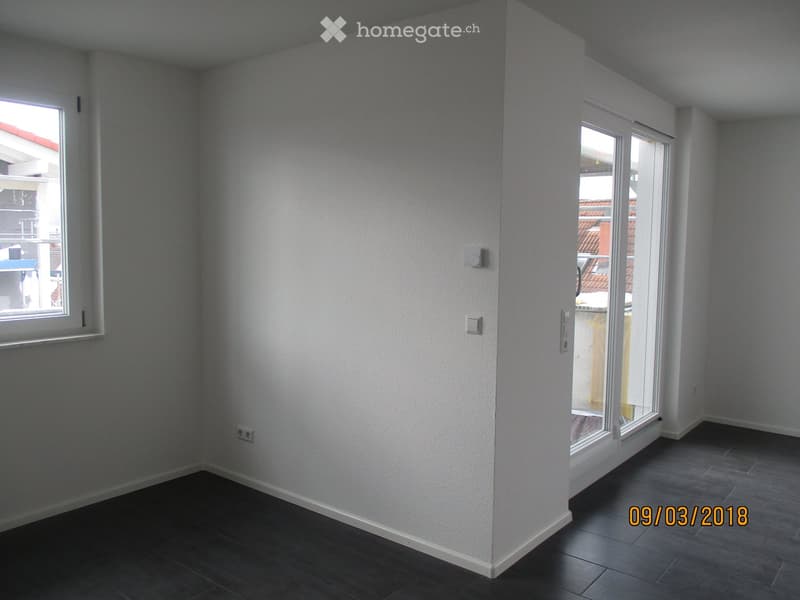 Empty room with light grey walls, dark tiled floor, and large windows with white frames. No furniture or equipment present.