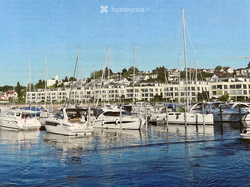A marina with several docked yachts and sailboats, surrounded by modern residential buildings and a clear blue sky.