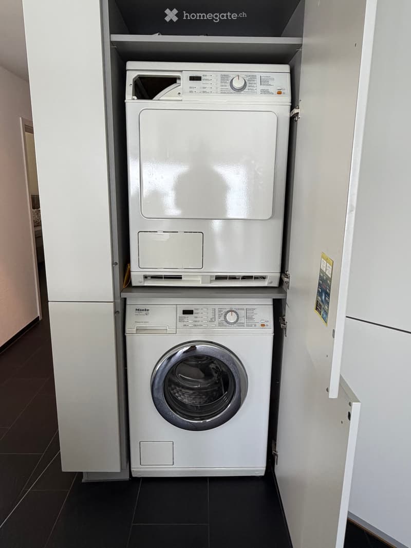 Compact bathroom with a white washing machine and dryer unit installed in a built-in cabinet.