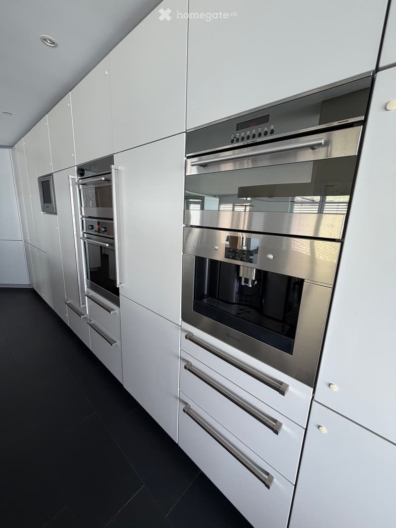 Modern kitchen with white cabinets, stainless steel appliances including an oven, microwave, and dishwasher, and black tiled flooring.