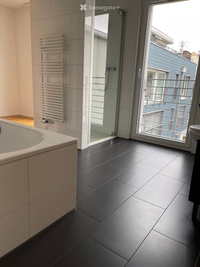 Bathroom with large bathtub, shower, white cabinets, and black tiled flooring.