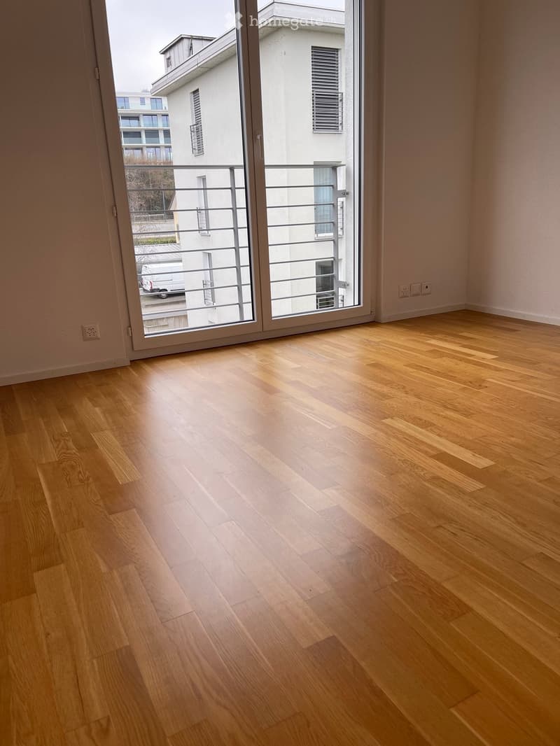 An empty room with sliding doors leading to the balcony, wooden floor, white walls, two power outlets