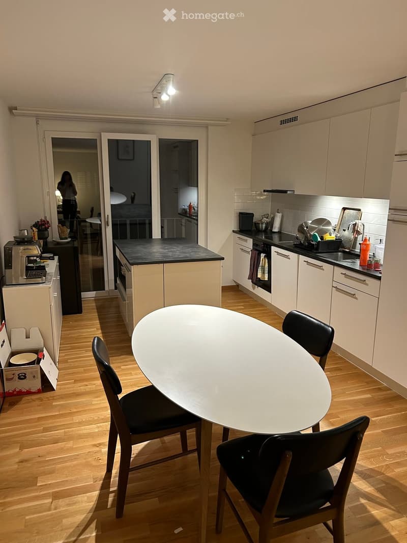 Modern kitchen with light wood flooring, white cabinets, black countertops, and a round dining table with four chairs.