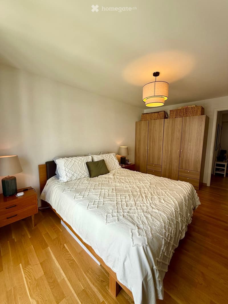 Well-lit bedroom with a large bed, nightstands, lamps, and a wardrobe with baskets on top.