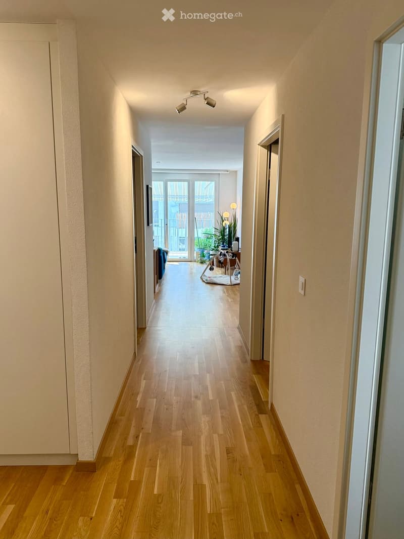 Long hallway with wooden flooring, recessed ceiling lights, and open doors leading to other rooms.
