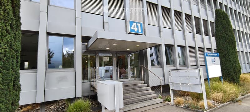 Modern building entrance with glass doors, steps, and mailboxes, featuring a sign displaying the number 41.