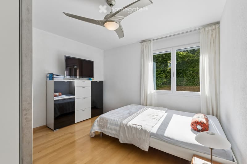 Modern bedroom with a large bed, nightstand, lamp, television, wardrobe, and large window with curtains.