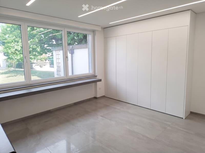 Empty room with white walls, large windows, built-in white cabinetry, and tiled floor.