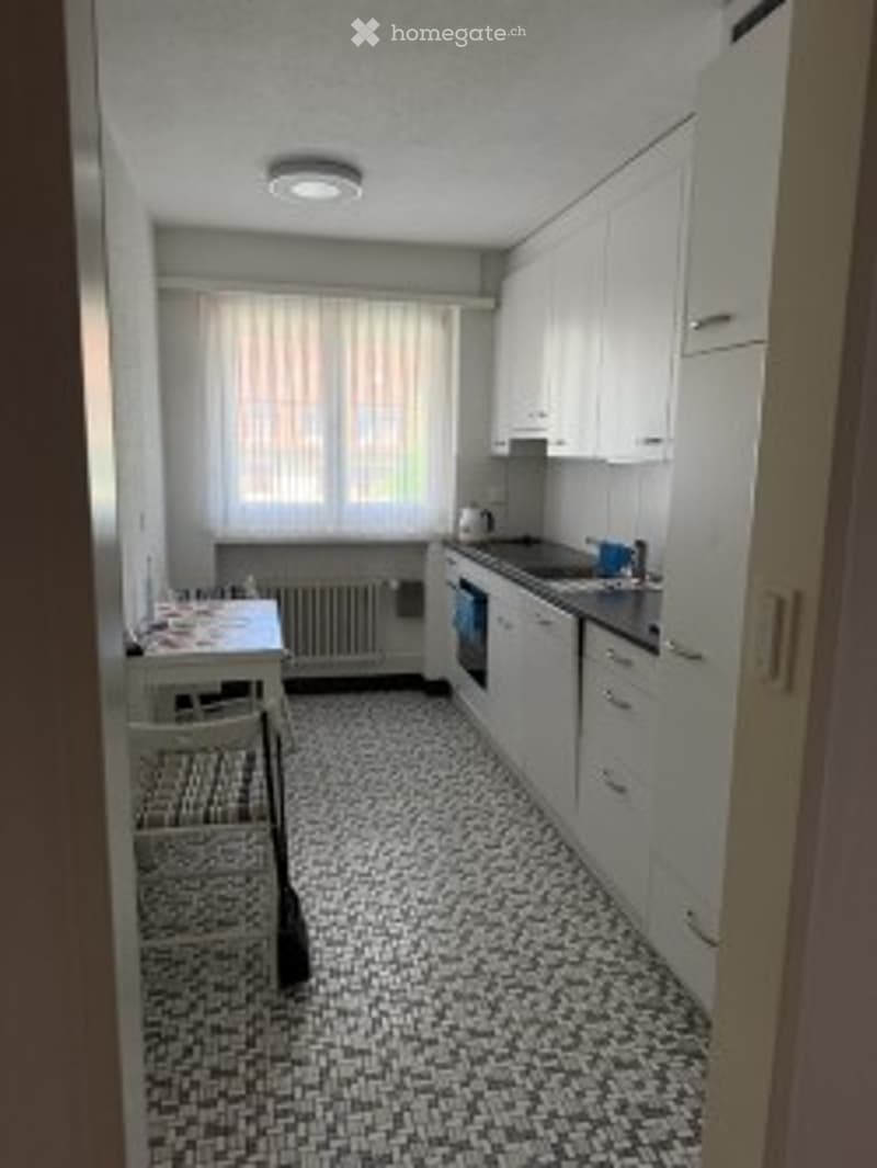 Modern kitchen with white cabinets, black and white tiled floor, a sink, an oven, and a small dining area with a table and chairs.