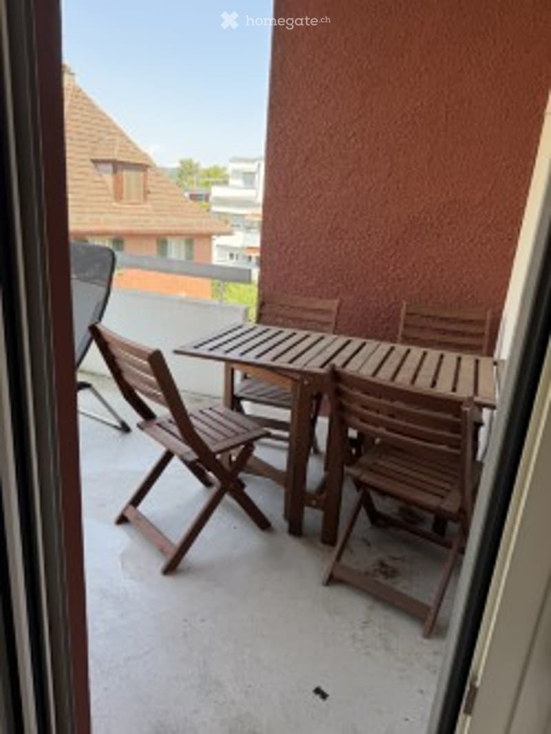 Balcony with wooden table and chairs, overlooking neighboring buildings.