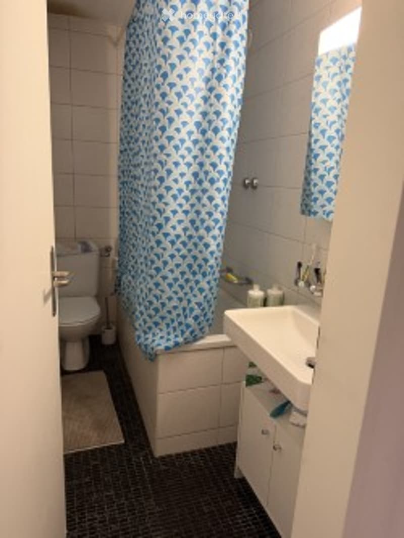Modern bathroom with white tiles, a blue shower curtain, a toilet, a bathtub, a sink, and a mirror.