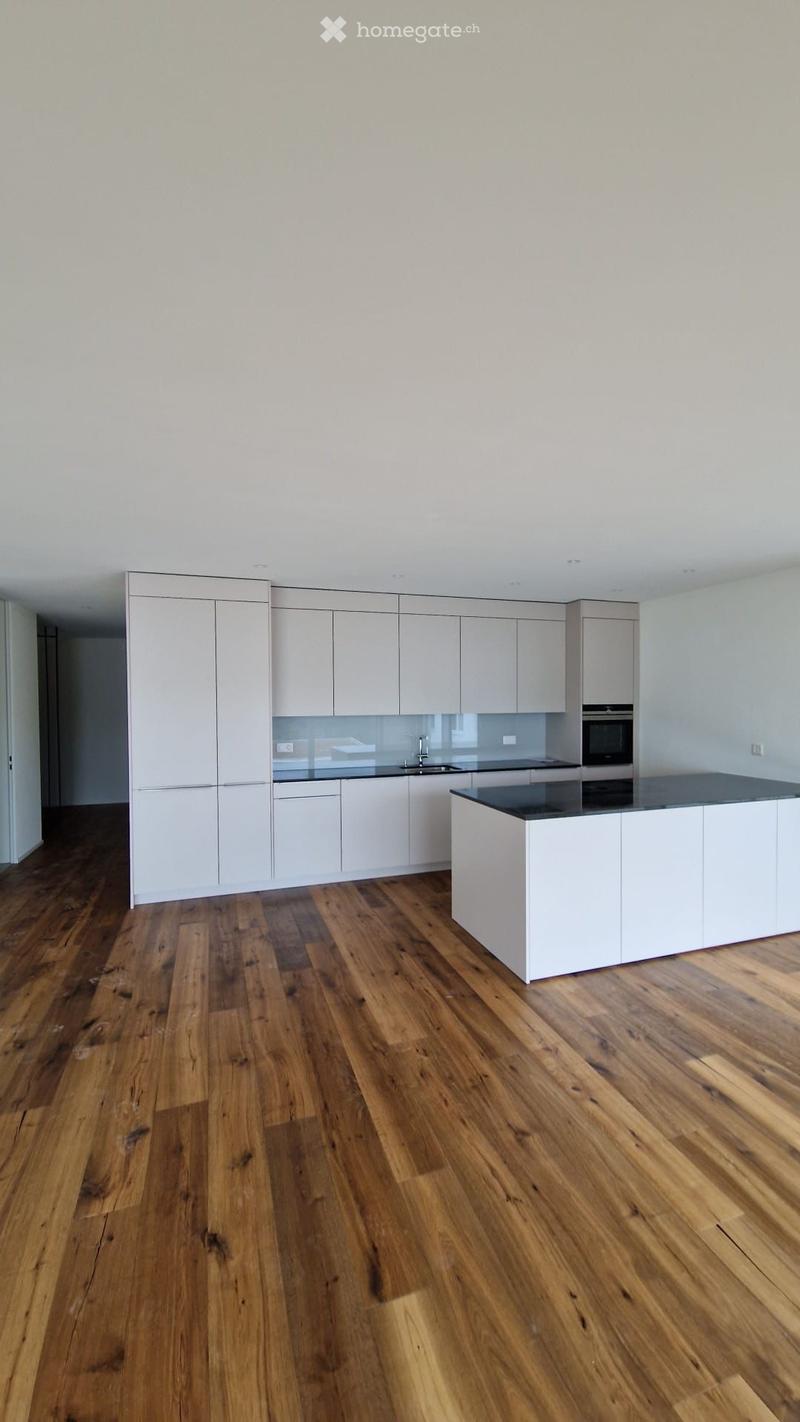 Empty kitchen with white cabinets, a black countertop, and wooden flooring.