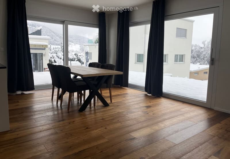 Dining room with wooden floor, large windows, and a dining table with chairs.
