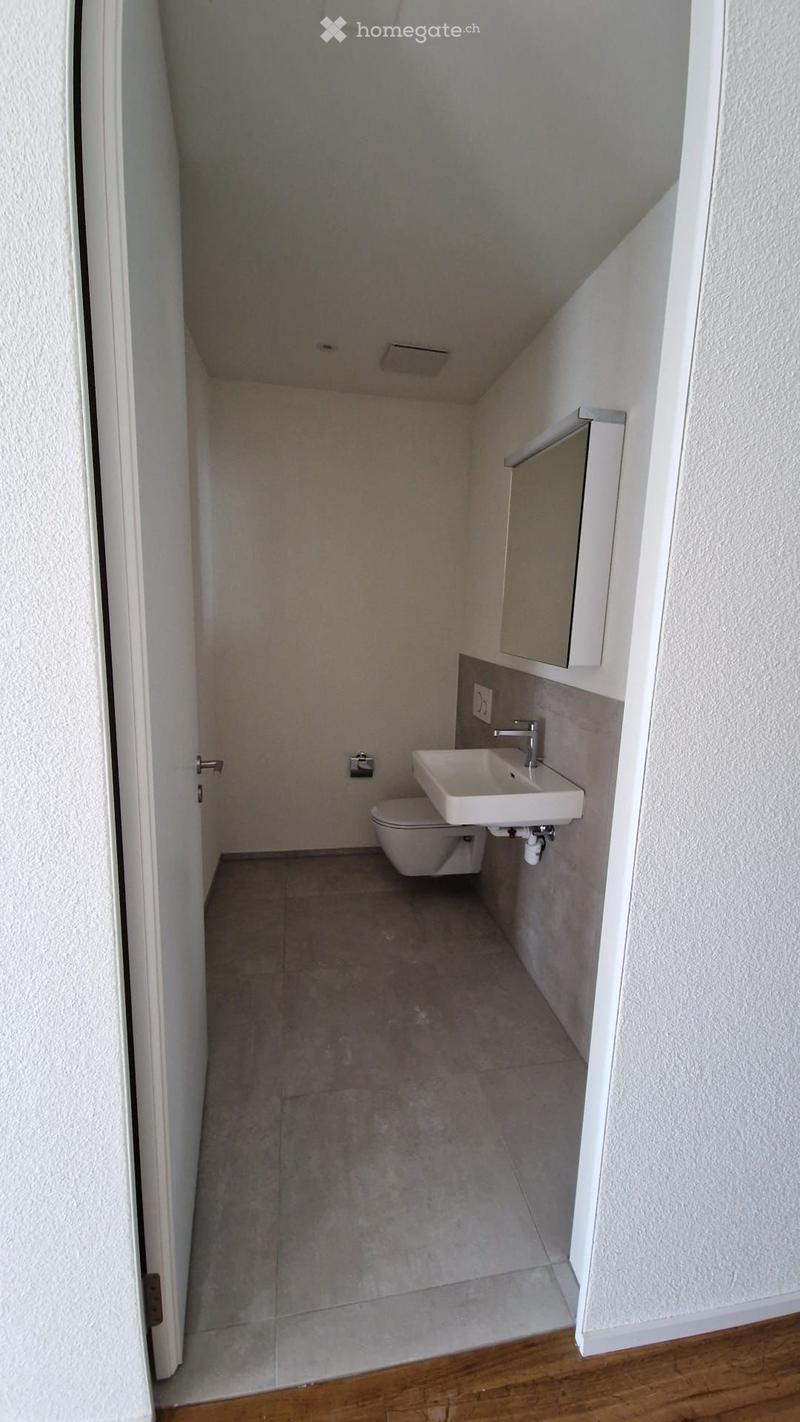Small, modern bathroom with a toilet, sink, and mirror. The walls are white, and the floor is tiled.