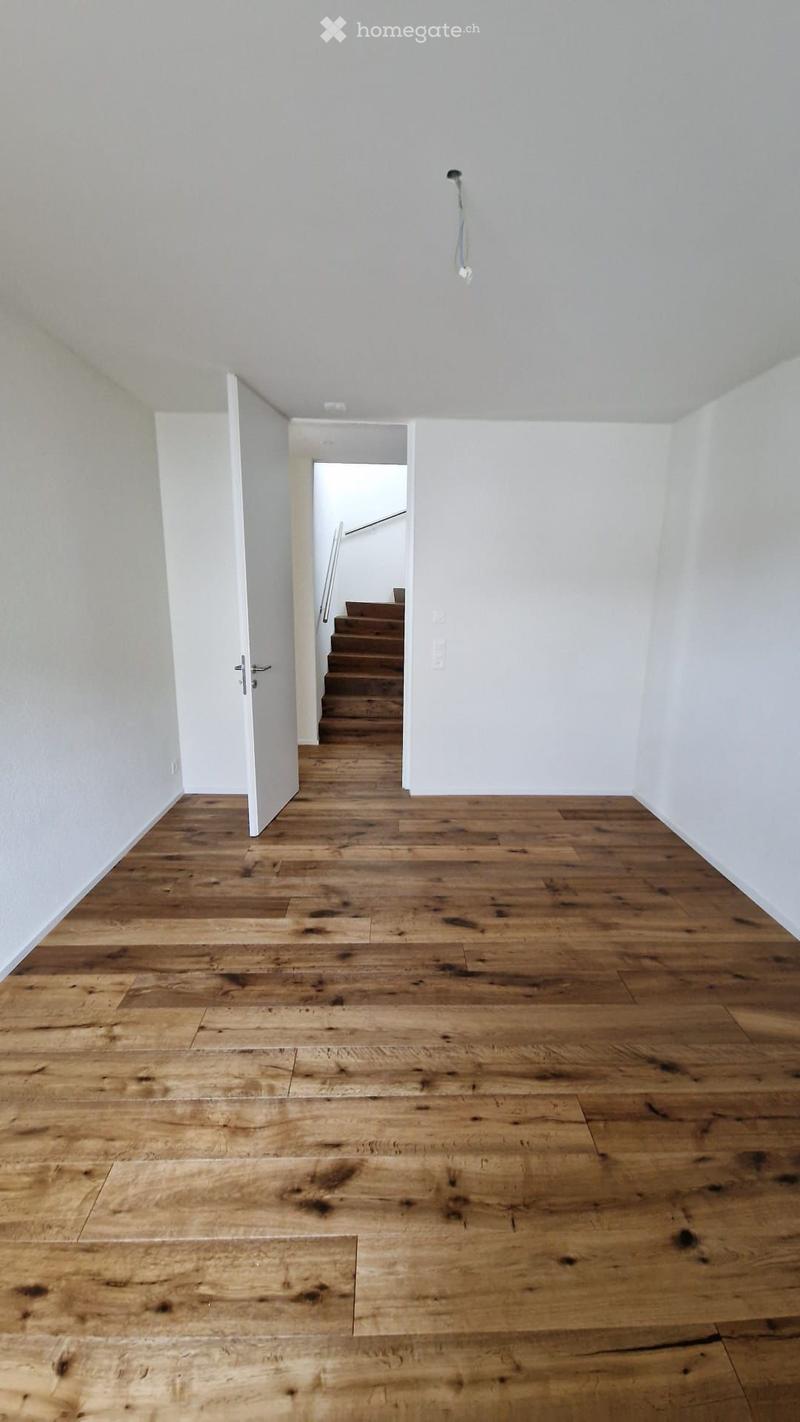 Empty hallway with wooden flooring, white walls, and a staircase leading upwards.