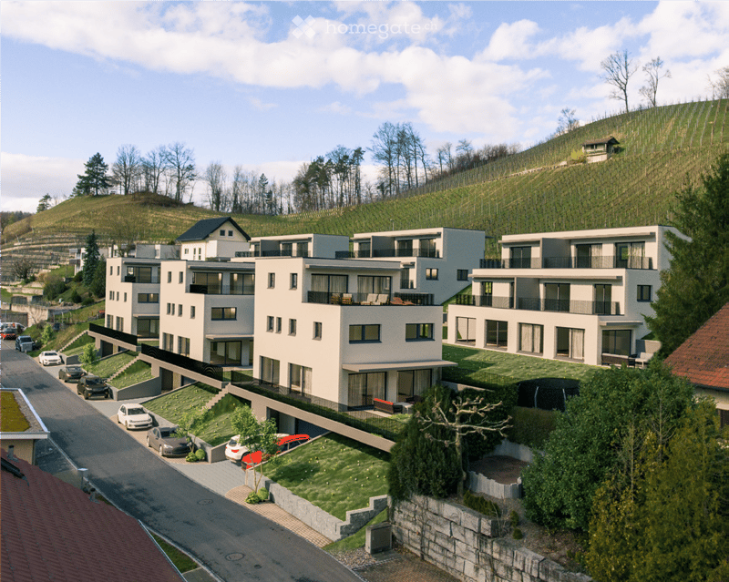 Modern multi-story residential building with balconies, surrounded by greenery and parked cars.