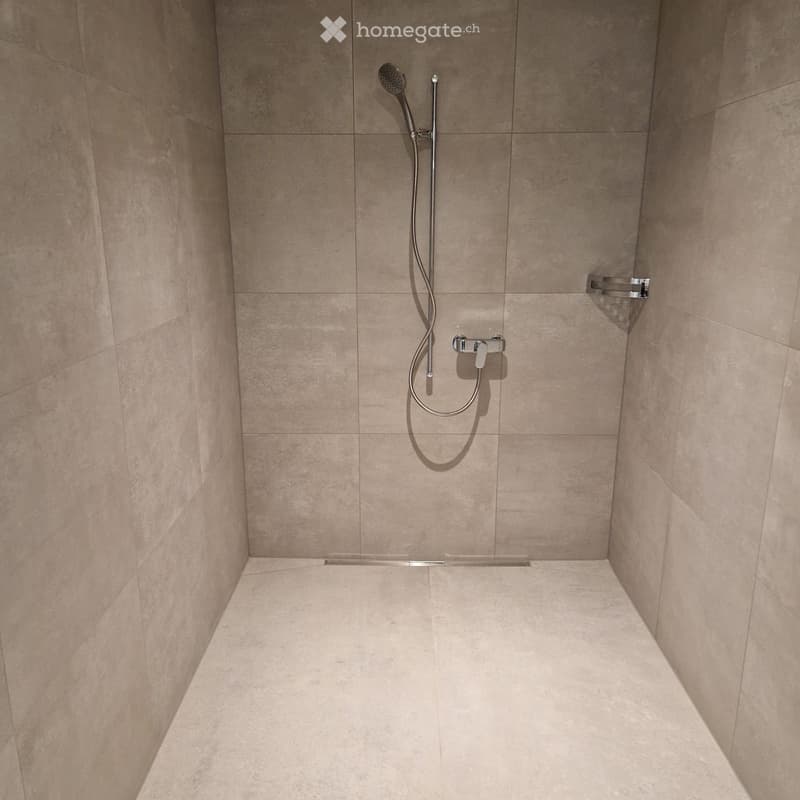 Modern shower area with beige tiled walls and floor, featuring a handheld showerhead and a built-in shelf.