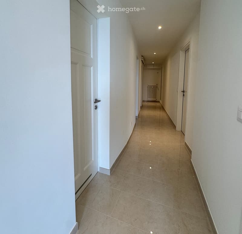 Empty hallway with tiled floor, white walls, and several closed doors on both sides.